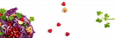 Colorful salad with red cabbage, pomegranate, walnuts, and fresh herbs arranged artistically on a white background